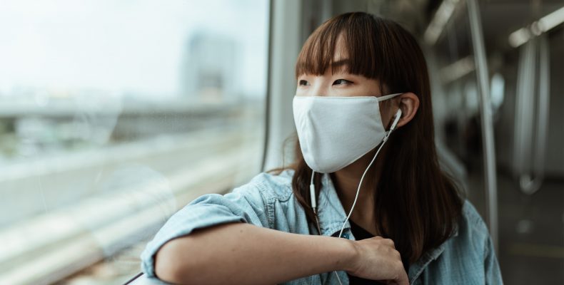 a young woman sitting on a train, wearing a face mask.