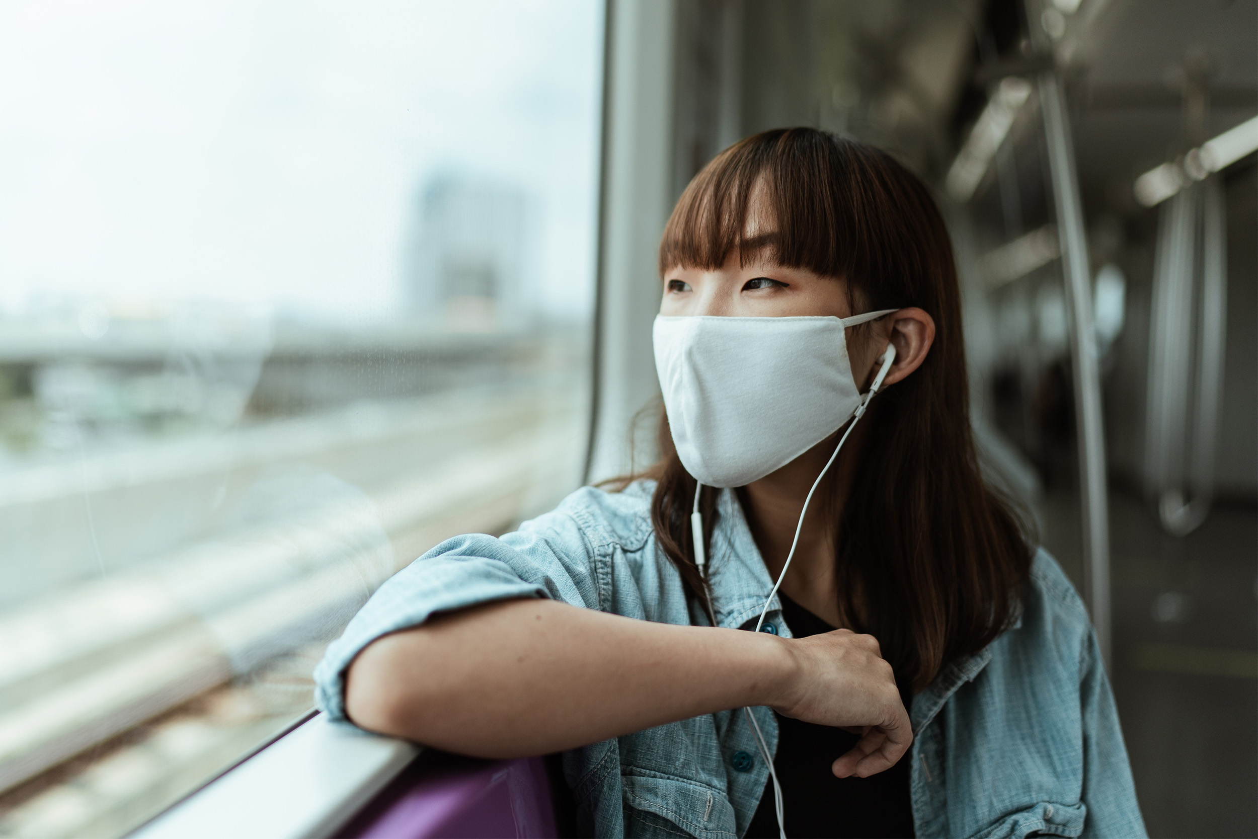 a young woman sitting on a train, wearing a face mask.
